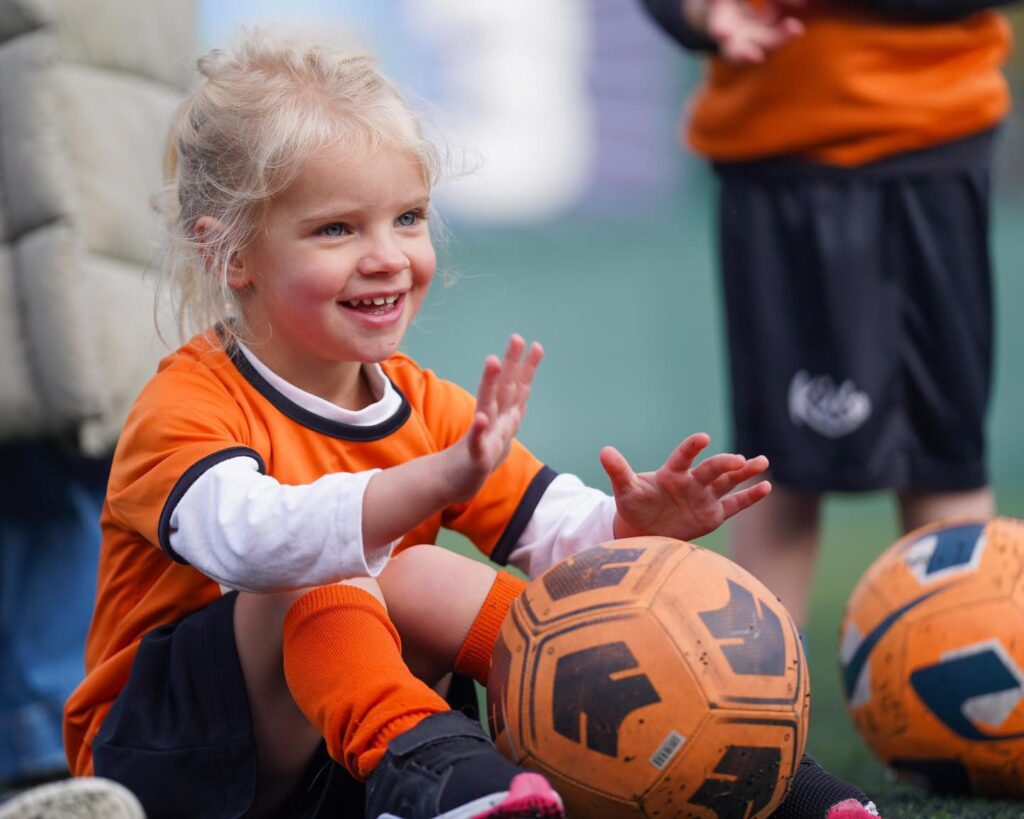 Image a young girl sat with a football for the blog The Essential Skills Your 3-Year-Old Will Master In Football Training